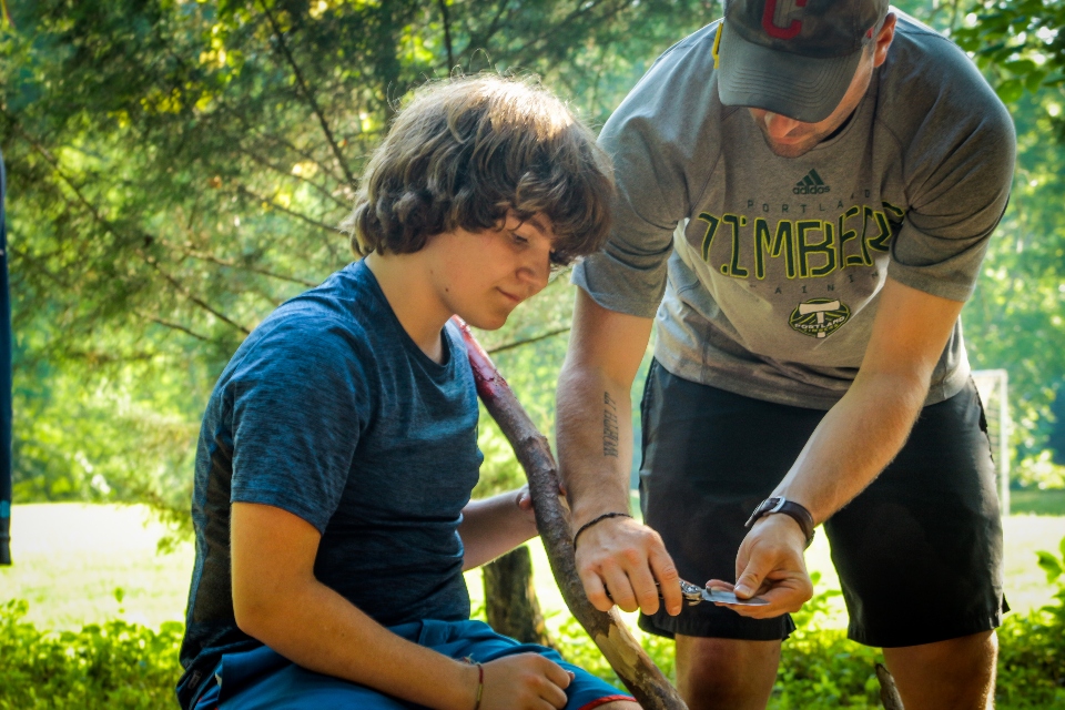 A counselor helps a camper carve his own walking stick for a hike around Virginia trails.